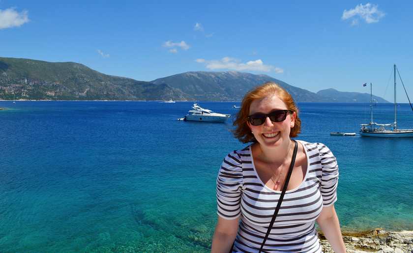 Mel smiling in a stripped top with blue water in Kefalonia and boat behind her