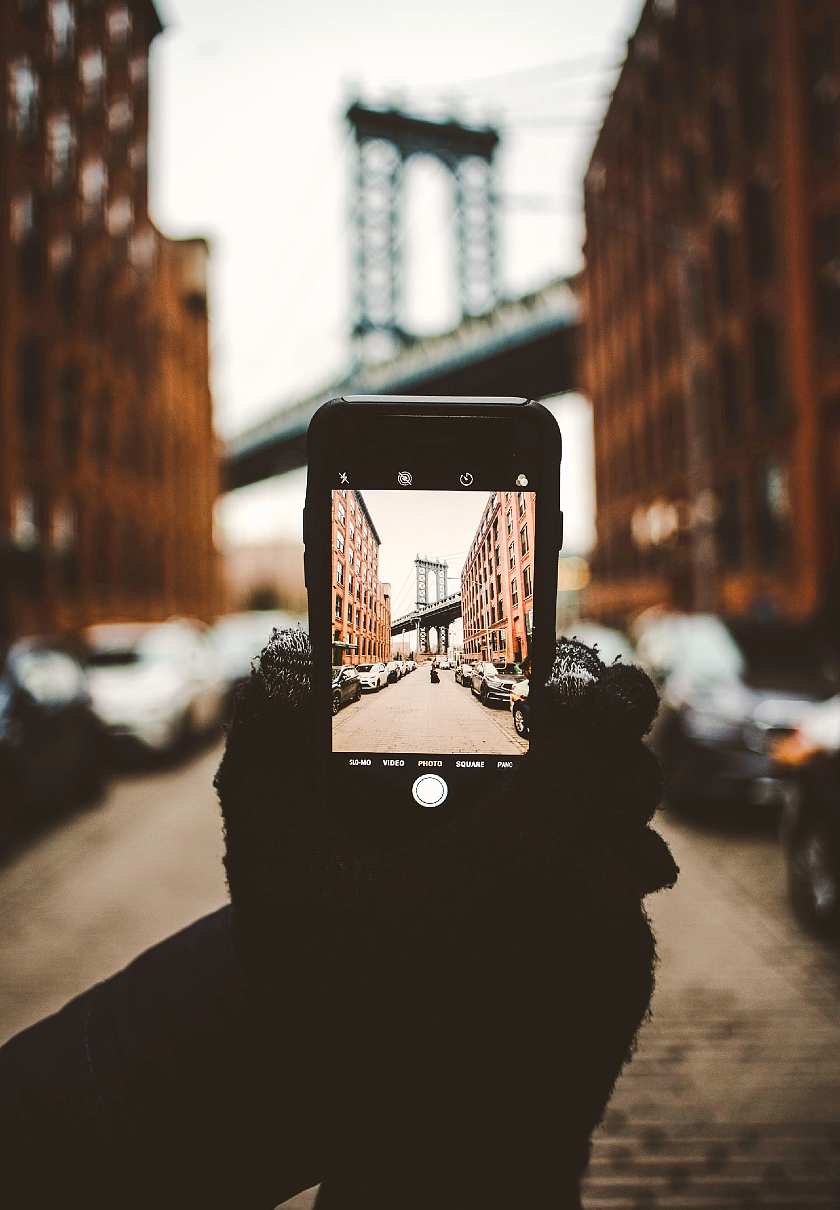 Gloved hand holding a phone focussed in on a picture of the Brooklyn Bridge and apartment buildings either side