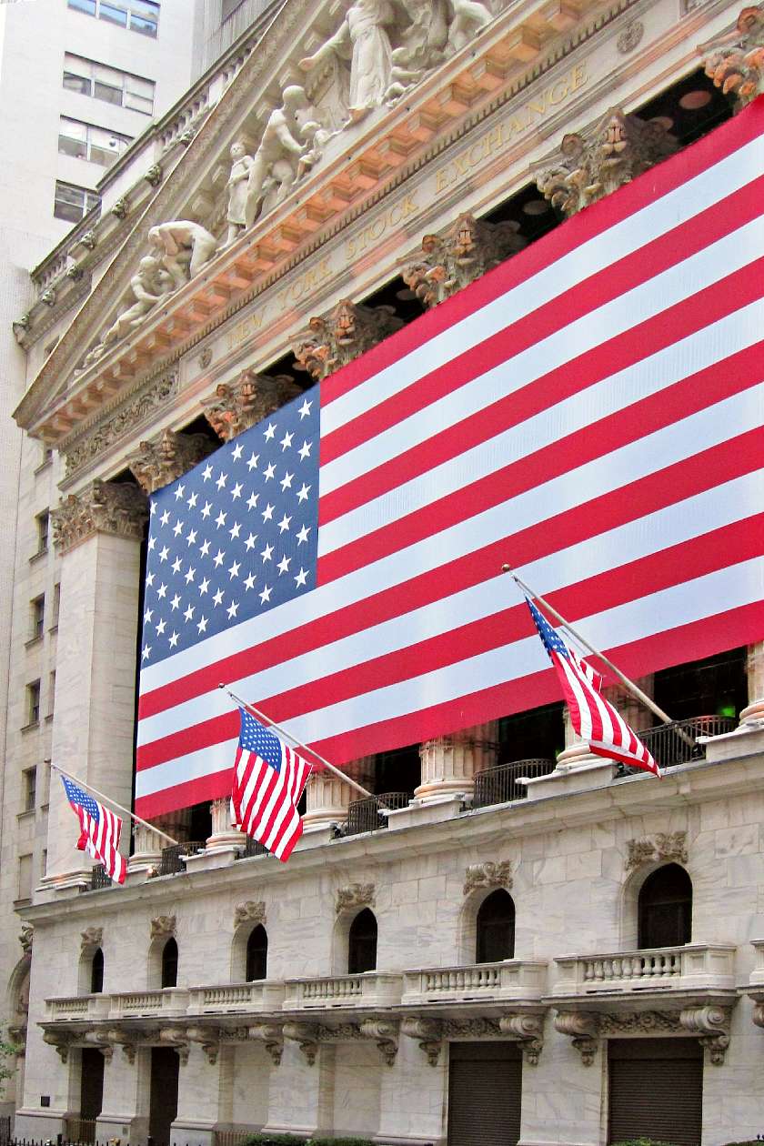 New York Stock Exchange building on Wall Street with a large USA flag across the front