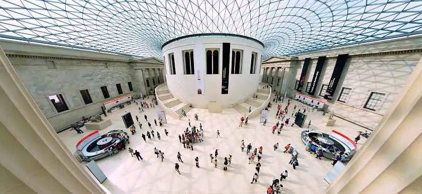 Inside the British Museum in London, a large white marble room with a glass roof and people walking around below