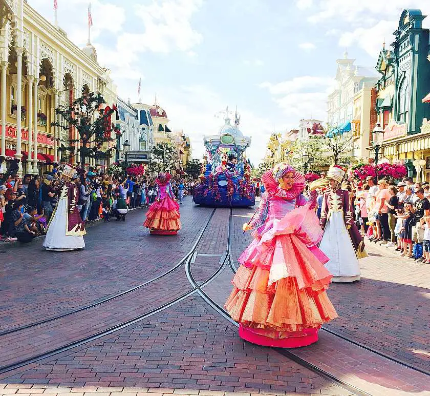 Disney parade with floats and ladies wearing colourful dresses walking down Main Street in Disneyland Paris