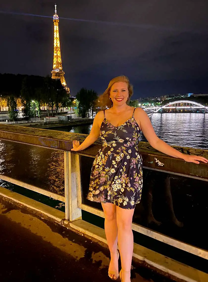 Mel posing in front of the Eiffel Tower at night wearing a blue dress with flowers on it for a night out