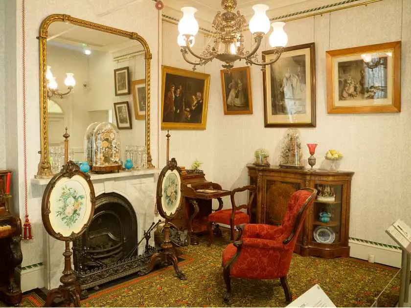 Inside a Victorian living room with paintings, a fireplace and a mirror in London's Geffrye Museum