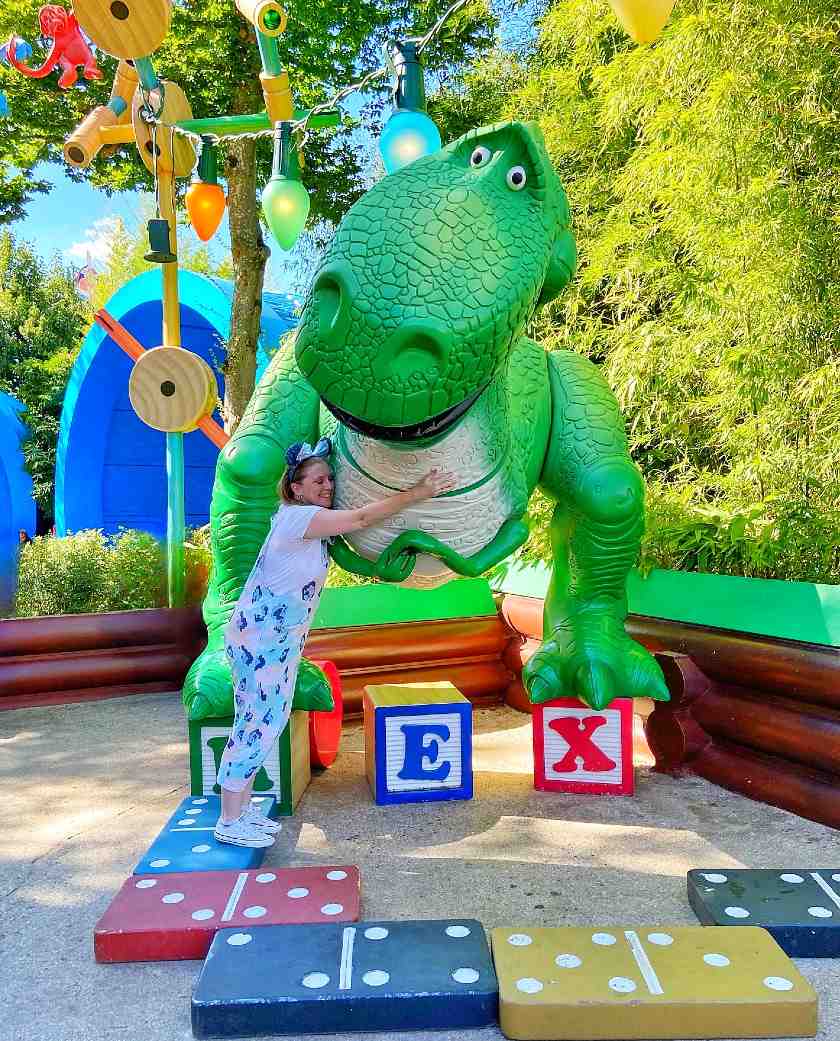 Mel hugging Rex the dinosaur from Toy Story stood on some giant colourful dominoes at Toy Story Land in Disneyland Paris