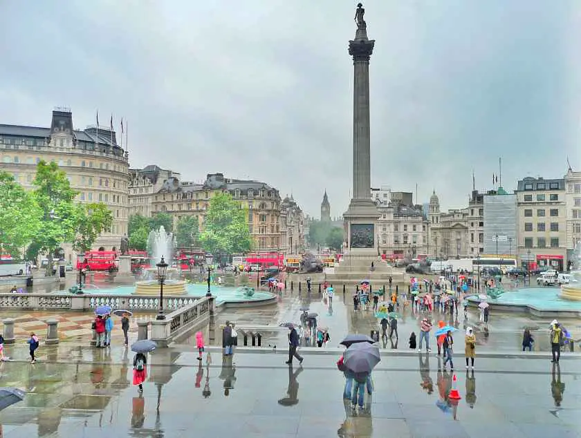 Trafalgar Square in London with Nelson's column in the background with lots of people holding up umbrellas in the rain