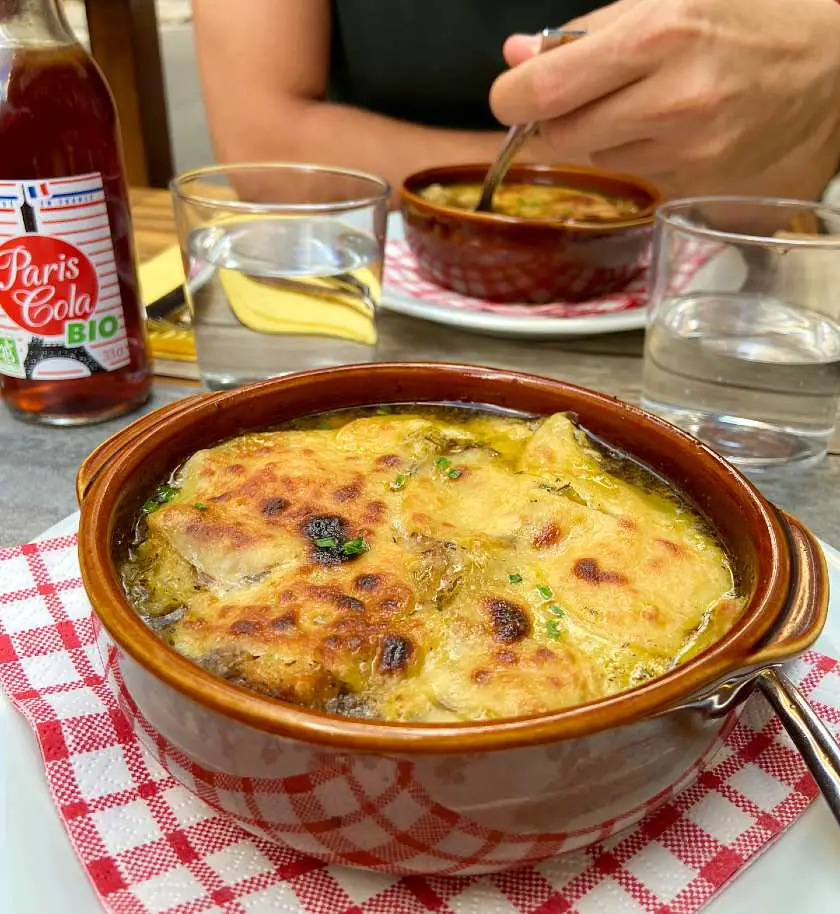 Casserole dish with vegan onion soup in it with a layer of vegan melted cheese on top at vegan restaurant le Potager du marais 