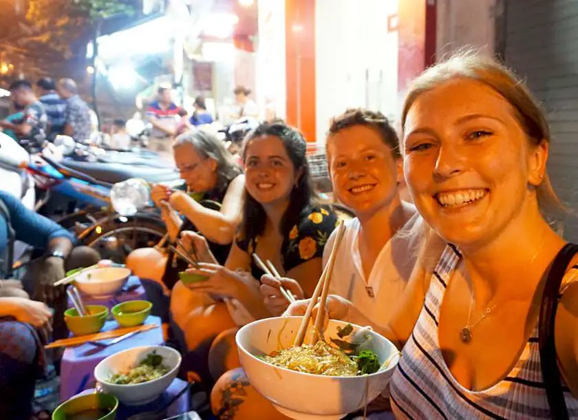 Mel from Footsteps on the Globe eating noodles on the streets of Hanoi in Vietnam with friends