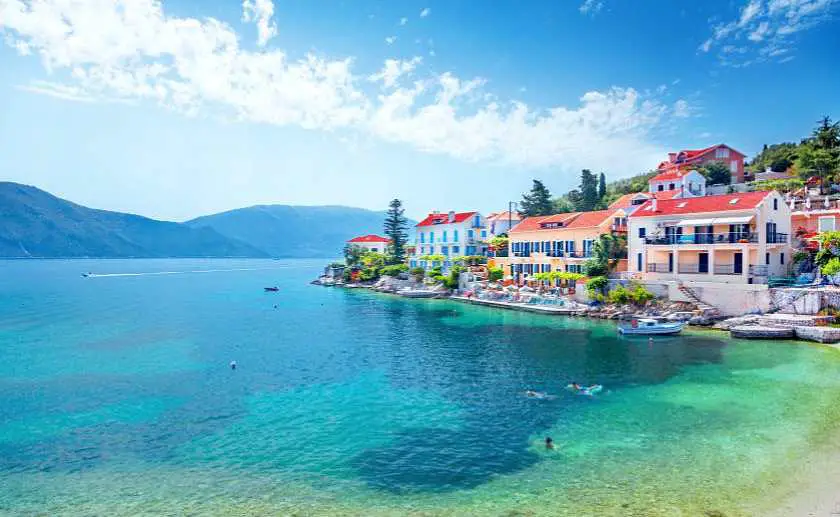 Fiskardo village in Kefalonia with boats and orange shaded buildings on the edge of the blue water