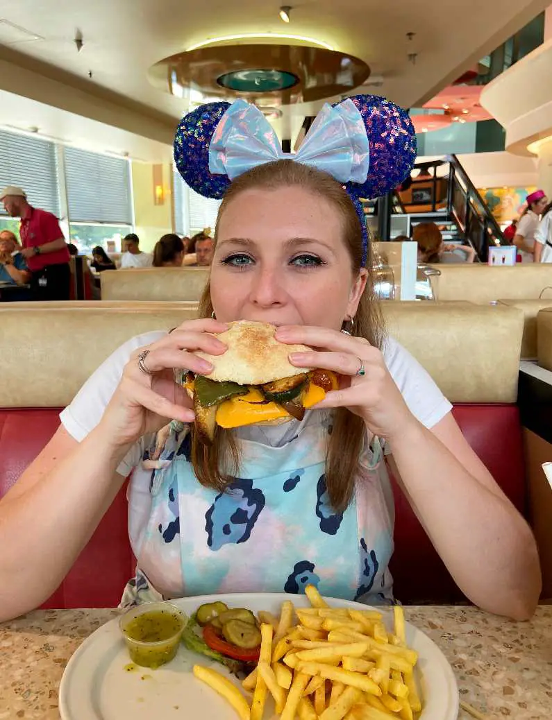 Mel wearing Minnie Mouse ears eating a vegan cheeseburger in Annette's Diner in Disneyland Paris 