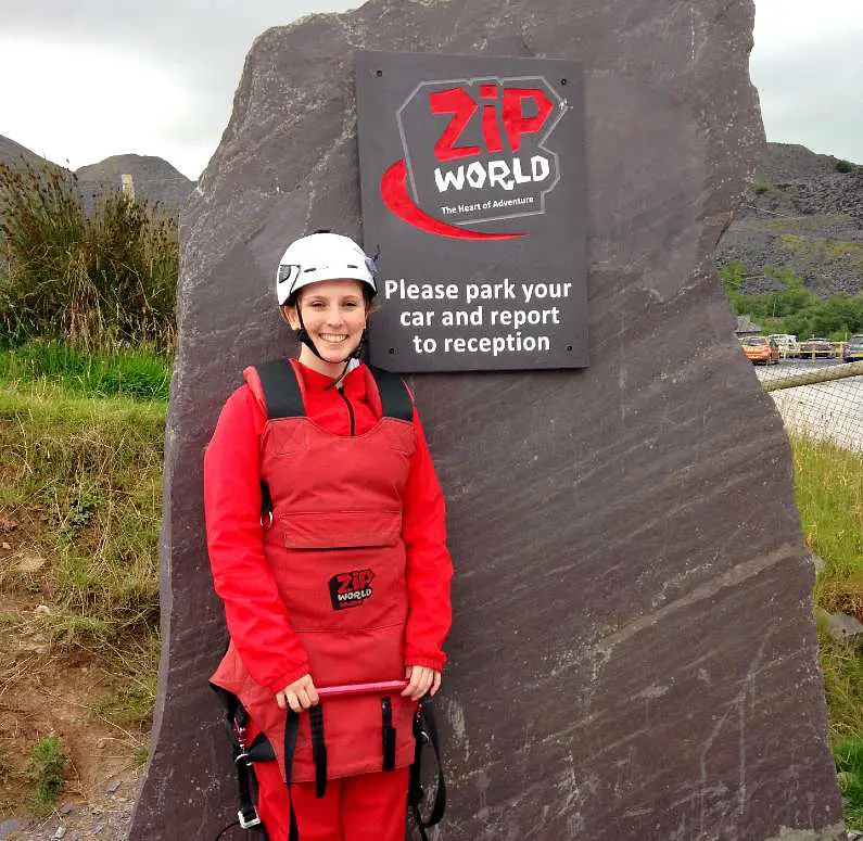Mel in front of the Zip World Slate sign dressed in her zipline suit and helmet ready to go