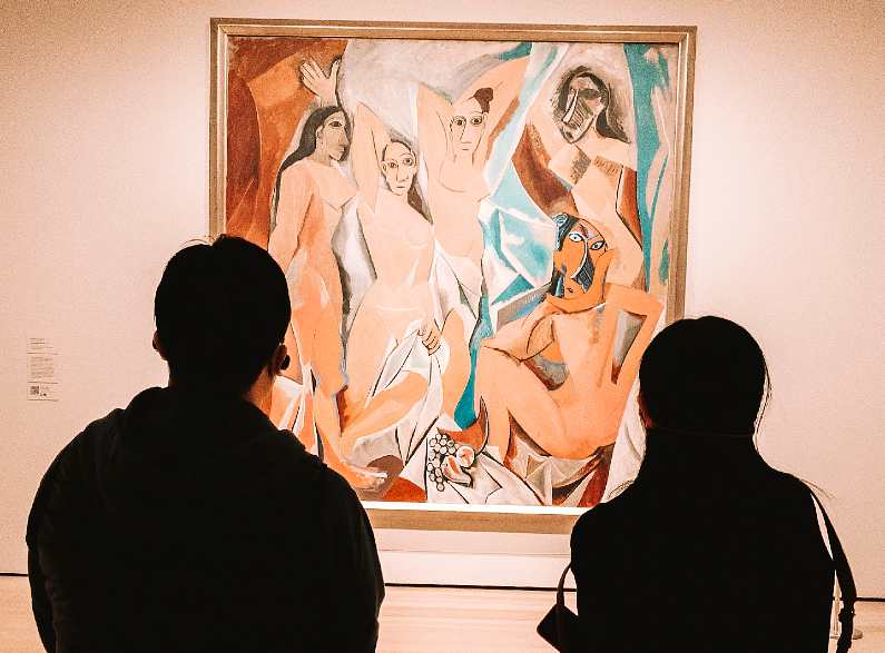 Two people looking at a Picasso painting of naked women