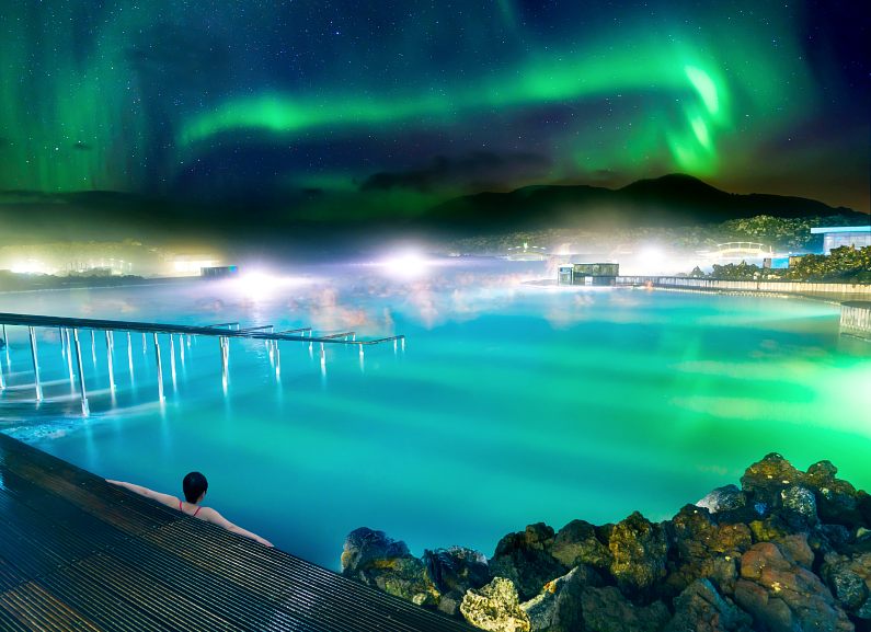 Dark haired woman watching the Northern Lights dancing above the Blue Lagoon at night