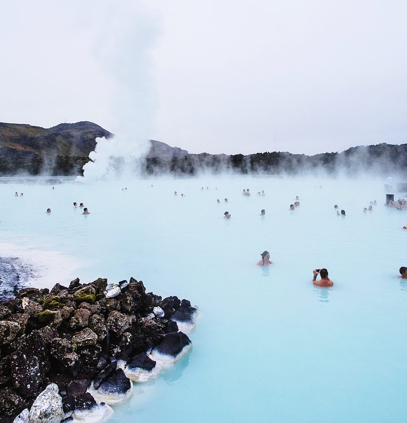 People swimming in the Blue Lagoon with white smoke coming off the water 