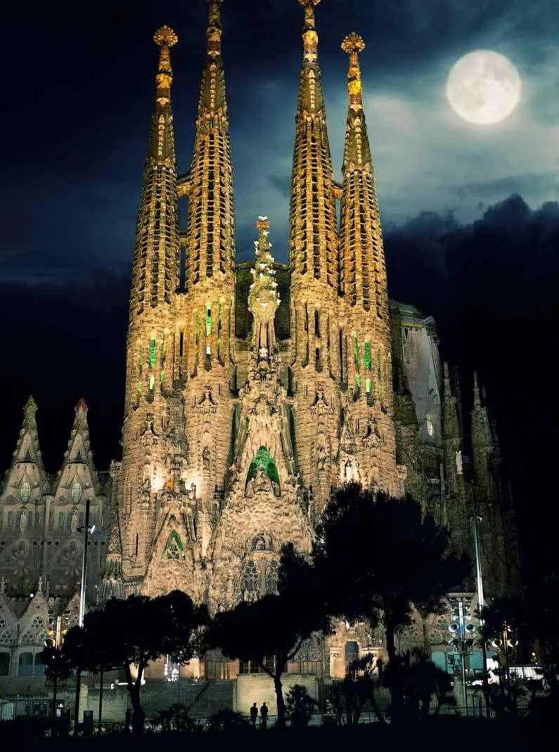 Outside the Sagrada Familia lit up at night with a full moon in the background
