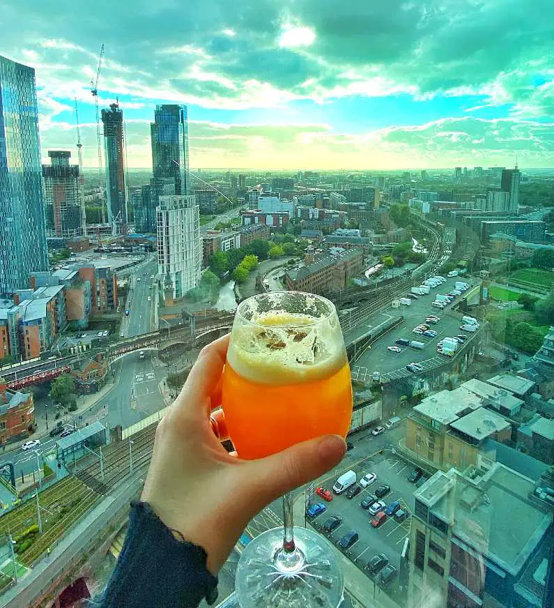 Skyline of Manchester from the window of the bar Cloud 23 with an orange cocktail in being held up in the foreground