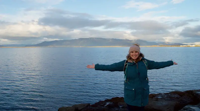 Mel with her arms out with Icelandic sea and mountains behind her