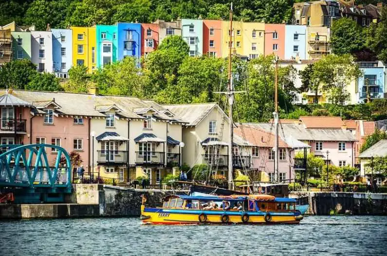 Bristol Harbour with candy coloured houses in the background and a yellow and blue boat sailing in the foreground