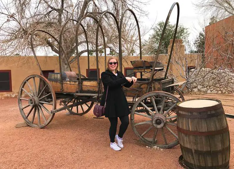 Mel in front of an old wagon pretending to ride a horse wearing a black coat and sunglasses