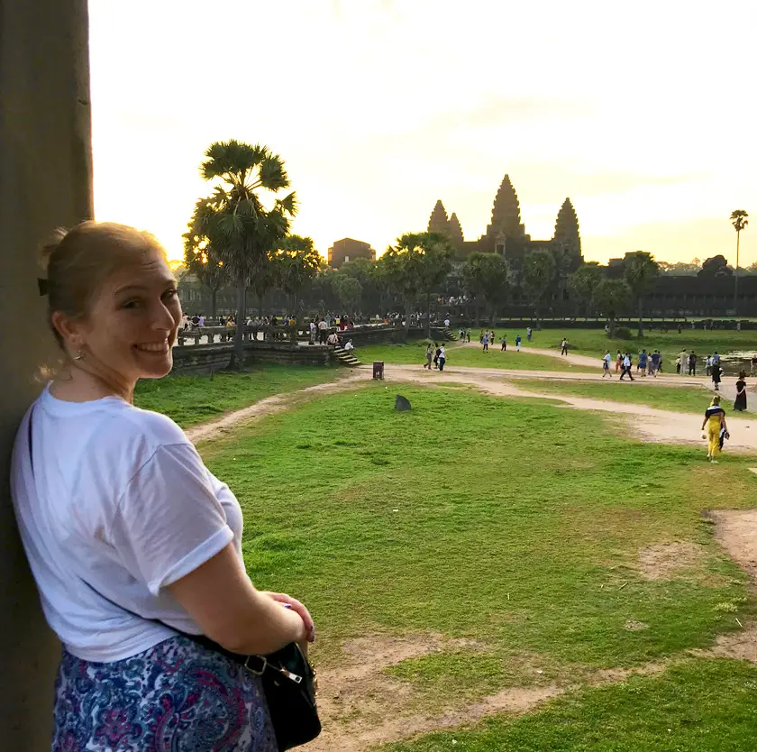 Mel from Footsteps on the Globe smiling from over her shoulder in front of Angkor Watt in Cambodia at sunrise, Breaking up, backpacking and beginning again 