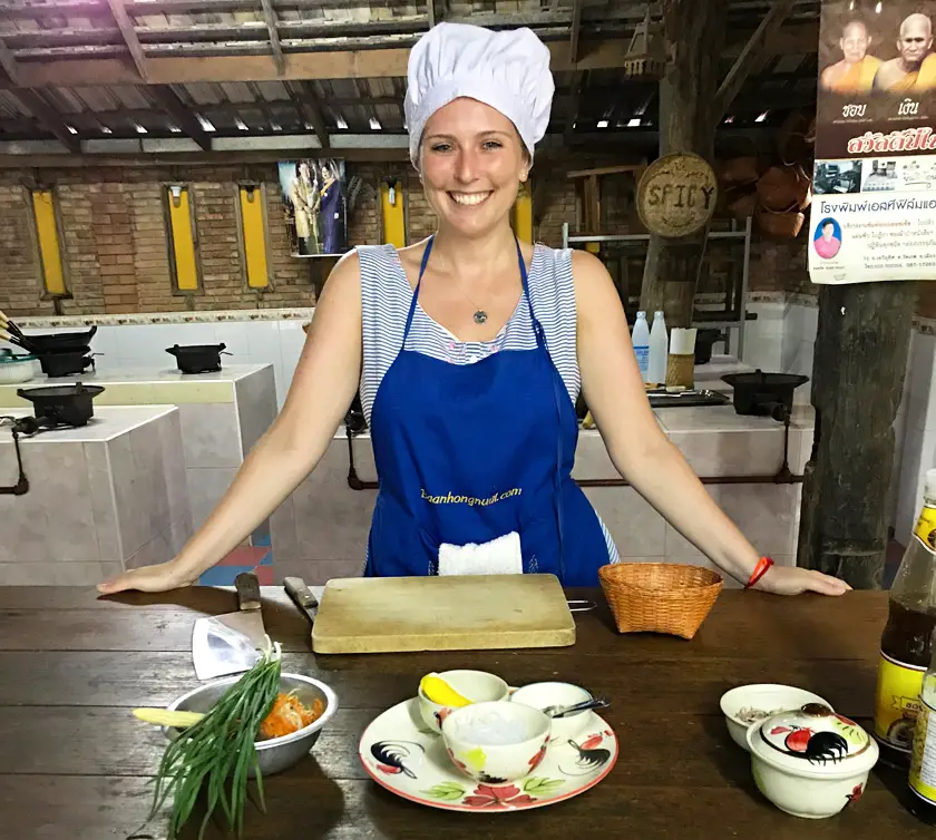 Mel in the kitchen at a cooking class wearing a blue apron and white chef's hat 