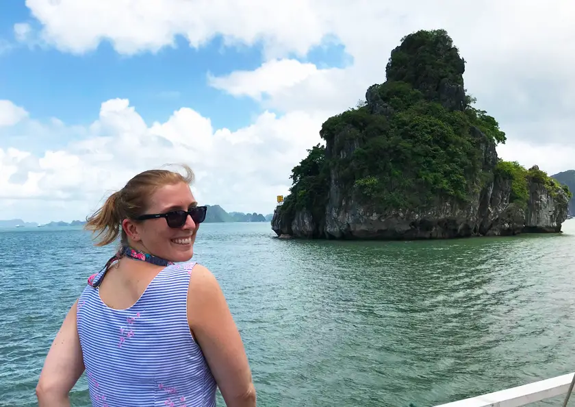 Mel from Footsteps on the Globe looking over her shoulder on a boat in front of Halong Bay in Vietnam wearing a blue dress