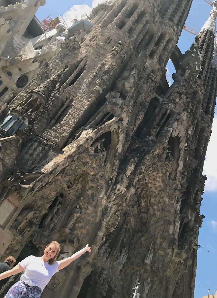 Mel from Footsteps on the Globe smiling and holding her arms up in front of the Sagrada Familia in Barcelona Spain with a sunny blue sky, Breaking up, backpacking and beginning again, Breaking up, backpacking and beginning again