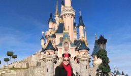 Mel from Footsteps on the Globe smiling in front of the princess castle in Disneyland Paris with a sunny blue sky, reasons to go to Disneyland Paris