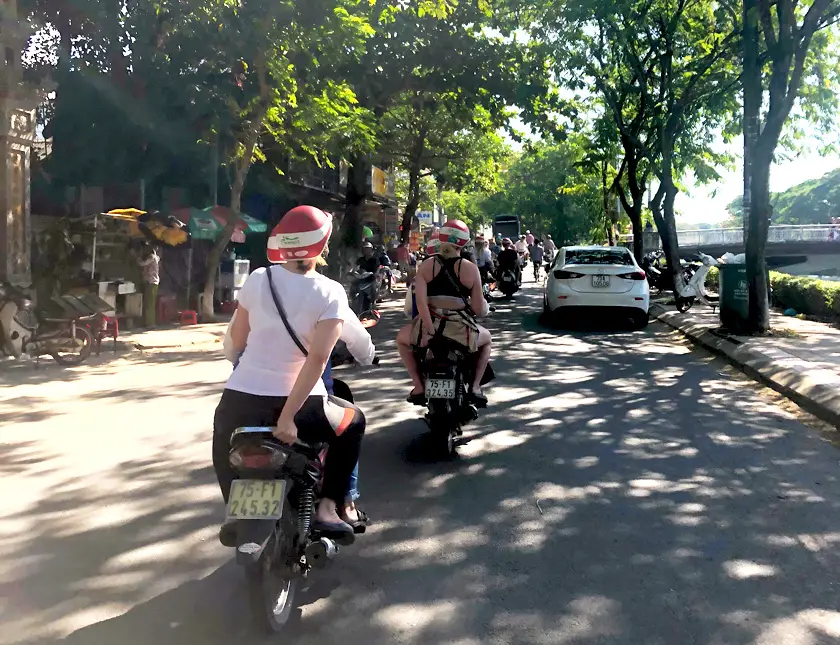 Mel from Footsteps on the Globe on the back of a motorbike driving down a busy street in Hue in Vietnam