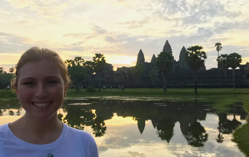 Mel from Footsteps on the Globe smiling in front of the temple and the lake at sunrise. 