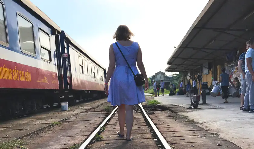Mel from Footsteps on the Globe walking away down the train tracks next to a train in Vietnam at sunset