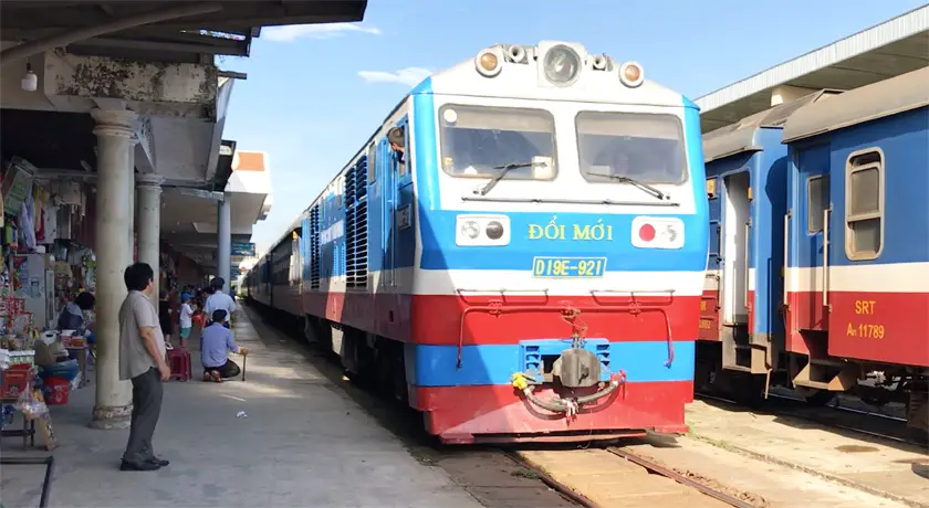 Blue, white and red train coming into the station in Vietnam with people waiting on the platform to board
