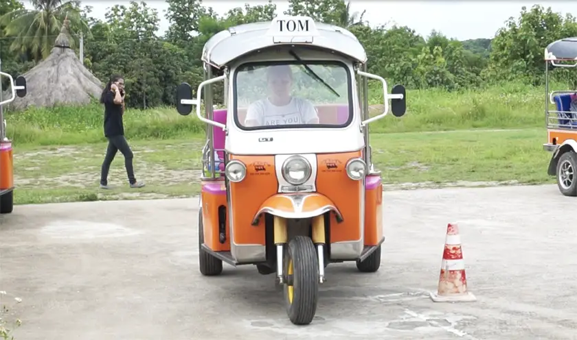 Mel from Footsteps on the Globe at the test centre driving an orange Tuk Tuk towards the camera with a cone on the right side of the Tuk Tuk