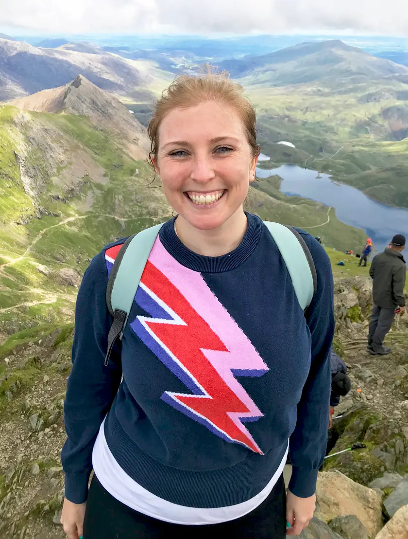 Close up image of Mel smiling from the top of Snowdon after reaching the top of the mountain wearing a David Bowie Style jumper.