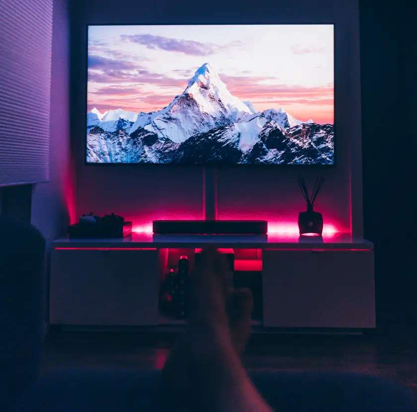 A dark room with a mountain on the tv screen and someone's feet in the foreground crossed