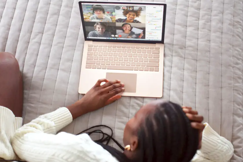 Woman in white laying on a bed zoom chatting with her friends on her laptop