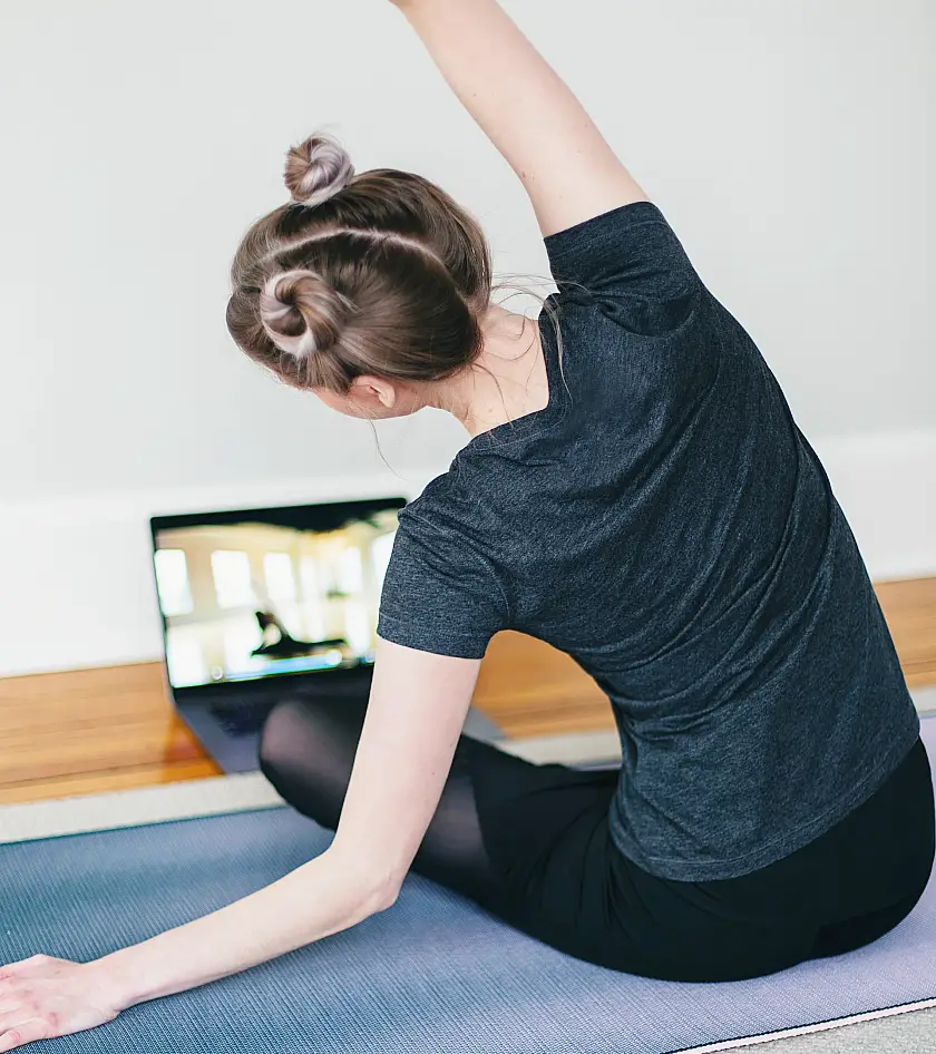 Woman wearing black stretching whilst following a workout video on her laptop