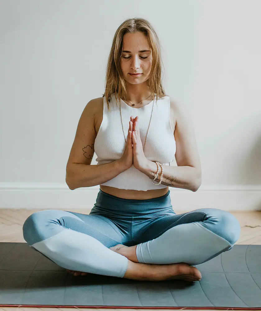 Blonde woman in a seated meditation position with her hands in a prayer position and her eyes closed
