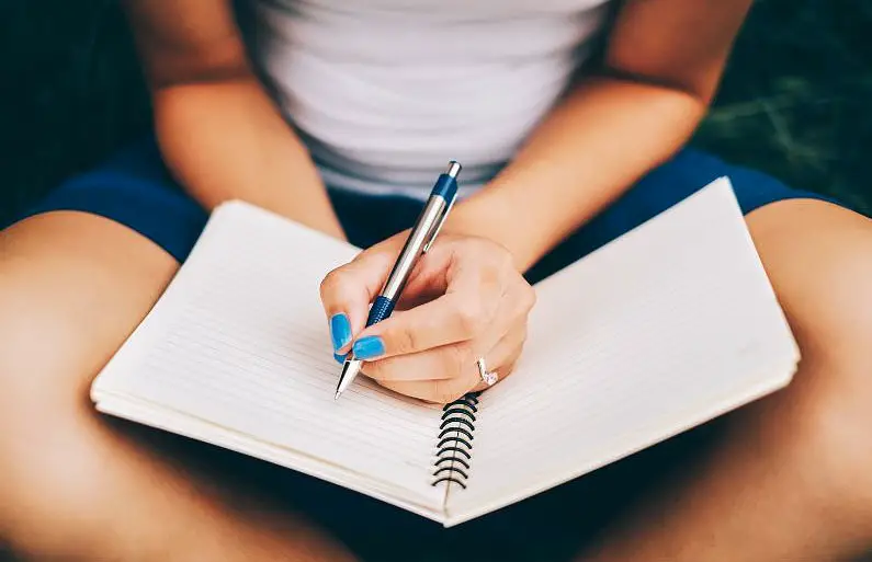 Woman's hand wearing blue nail varnish writing in an empty notebook