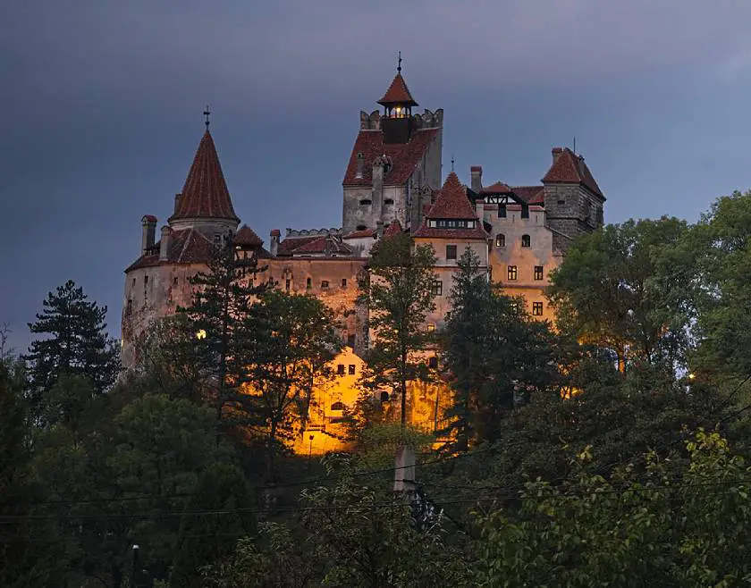 Bran Castle (Dracula's Castle) in Brașov, Translvania in Romania lit up at night amongst the some trees