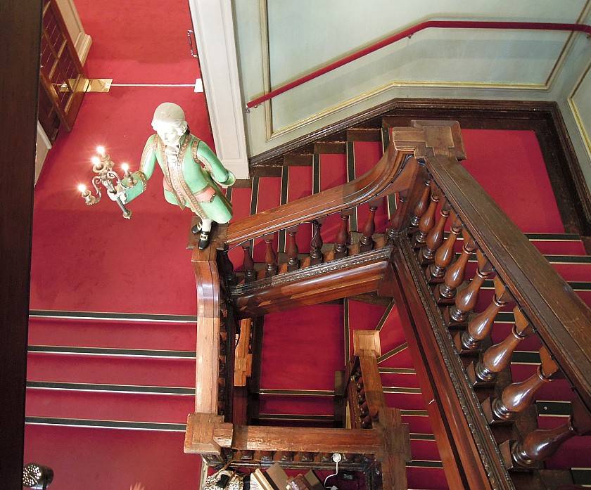 Looking down the wooden staircase in fortnum and mason with red carpet and wooden statue light fixture