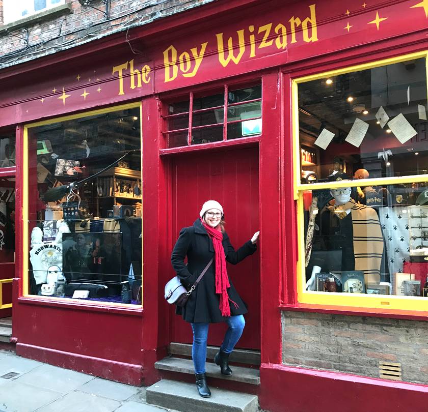 Mel stood outside 'The Boy Wizard' shop down The Shambles in York wearing a black coat, red scarf and pink wooly hat