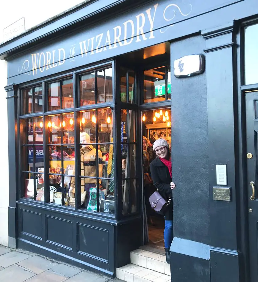 Mel peeking out from the 'World of wizardry' gift shop down The Shambles in York wearing a black coat, jeans and pink wooly hat