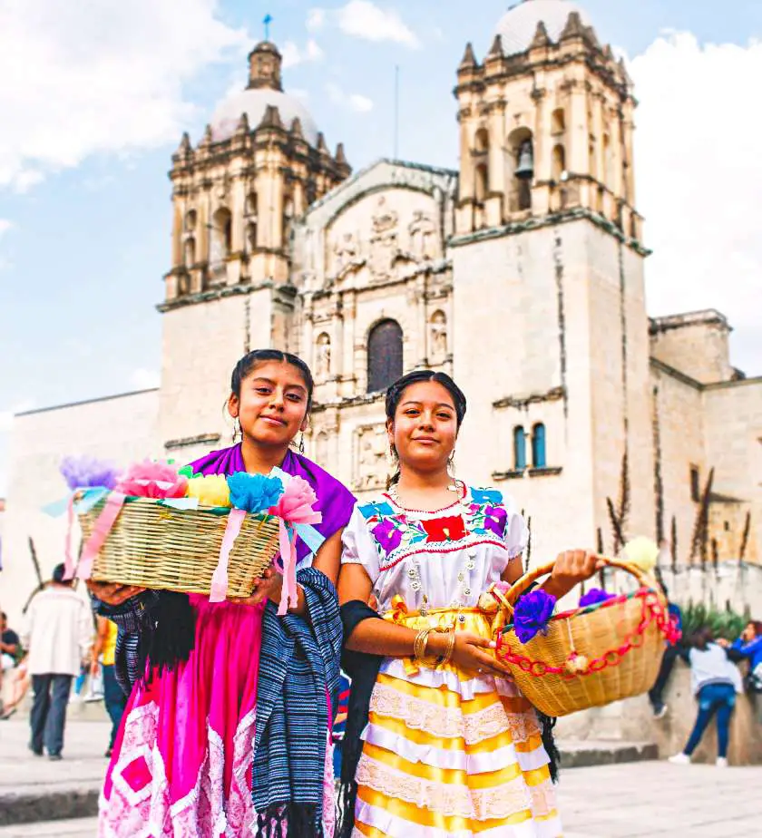 Two girls holding baskets with colourful decorations in the centre of Oaxaca, Mexico