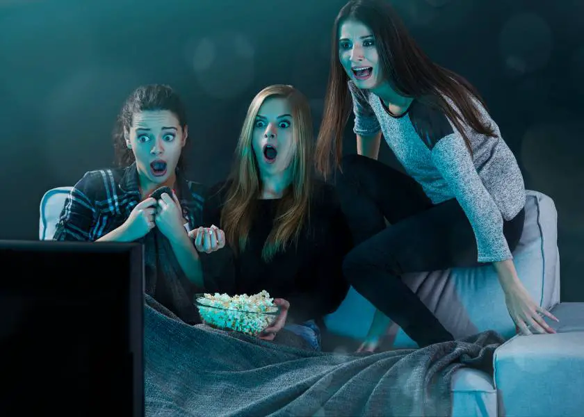 Three girls watching a horror movie at home with popcorn and getting scared