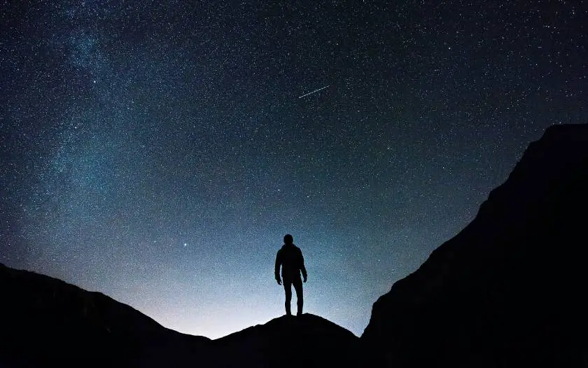 Person taking a spooky night hike looking up at the stars whilst hiking between two mountains