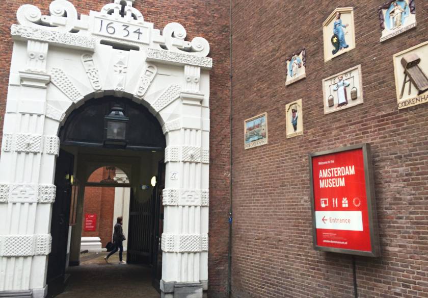 17th century white arch leading to the entrance of the Amsterdam Museum in Amsterdam with a sign on the wall for the museum
