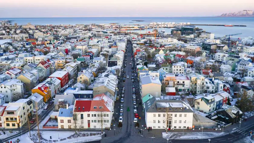 Rows of little white houses with colourful rooftops with the Icelandic sea and snow top mountains in the background