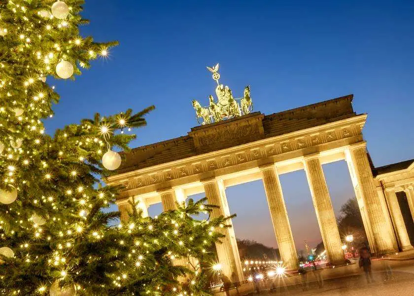Brandenburg Gate in Berlin at dusk with a Christmas tree and lights twinkling