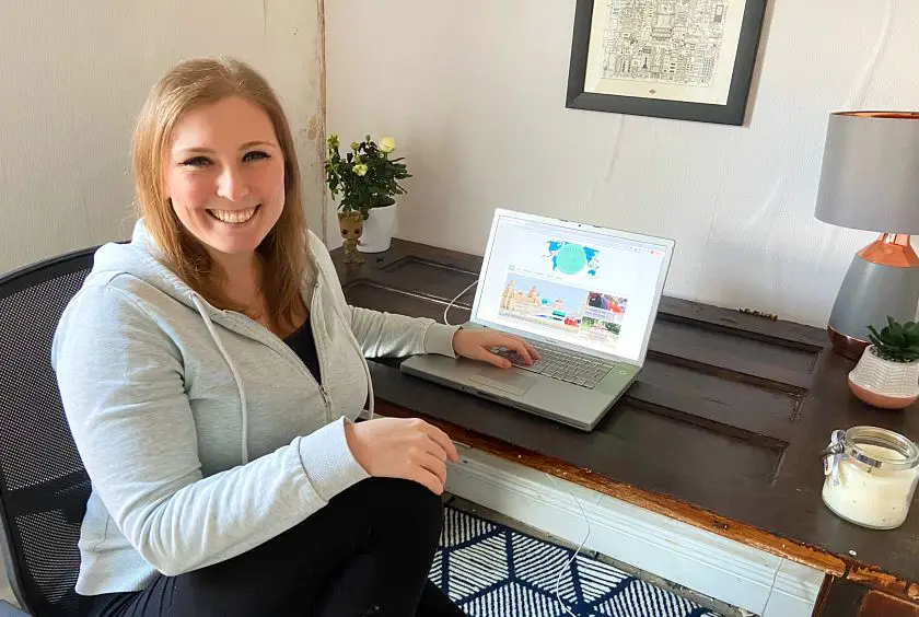Mel smiling sat at her desk using her laptop working on the Footsteps on the Globe blog
