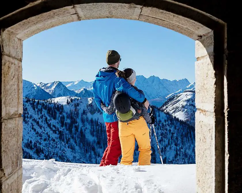 Couple with their arms around each other looking out whilst skiing over the french alps covered in snow